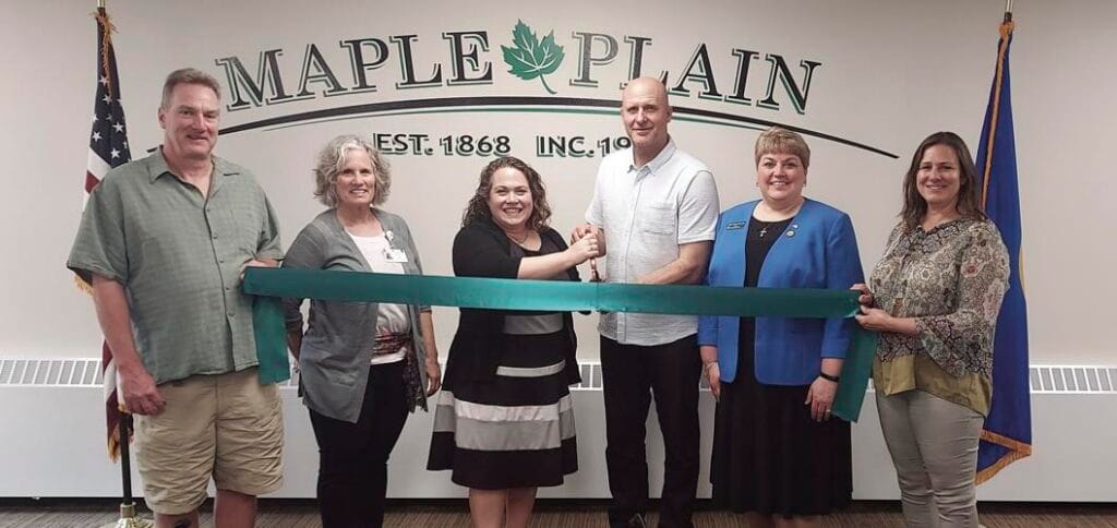 Group of WHCC members cutting a ribbon in the Maple Plain council chamber.